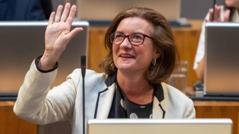 A smiling Eluned Morgan waving in the Senedd chamber