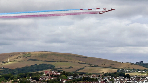 Nine Red Arrows planes flying over Swanage, with red, white and blue trails following their path.