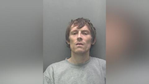 A custody picture of a man with messy dark brown hair, looking into the camera.