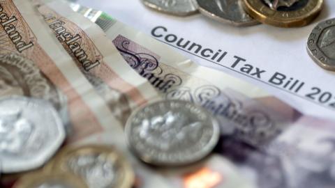 Coins and notes of various values sitting on top of a council tax bill.