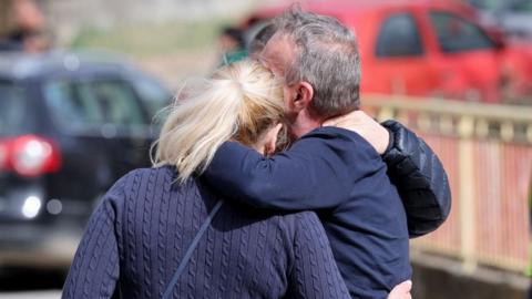 Three people with their backs to the camera have arms around each other outside a hospital in Kocani, North Macedonia, March 15, 2025