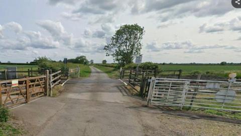 A level crossing on an isolated rural road. The crossing is open and surrounded by fences and gates. 