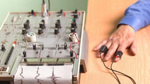A hand on a table connected to wires from a machine.