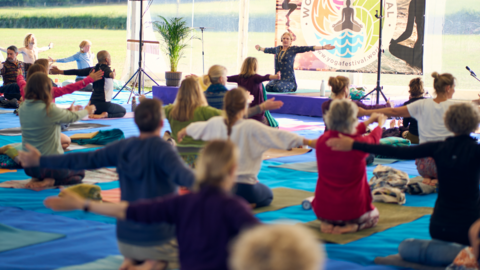 People in a marquee doing yoga and taking instructions from a teacher on a stage.