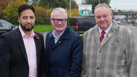 From left to right: Qaiser Azeem, Richard Parker and Stephen Simkins at Bilston High Street island, which has been resurfaced. They are all smiling at the camera and wearing suits, while cars and road signs are pictured behind them.