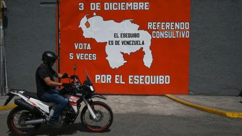 A man on motorcycle rides past a mural campaigning for a referendum to ask Venezuelans to consider annexing the Guyana-administered region of Essequibo, in 23 de Enero neighbourhood in Caracas on November 28, 2023.