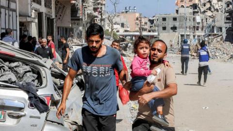 A man carries a child while evacuating the Jabalia camp for Palestinian refugees in the northern Gaza Strip on 9 October 2024 amid the ongoing war in the Palestinian territory between Israel and Hamas