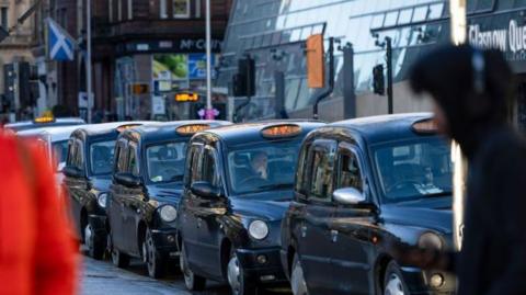 A row of black cabs sitting across from Queen Street train station