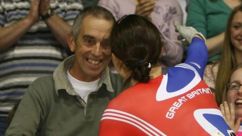 Victoria Pendleton is seen from behind in her racing outfit as she leans over the audience barrier to hug her father.