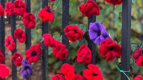 Close-up of homemade knitted poppies attached to an iron fence outdoors in nature for Remembrance Sunday.