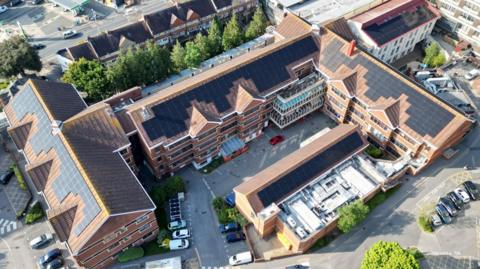 An aerial view of Poole Hospital. It is a brown brick building with solar panels on its roof.