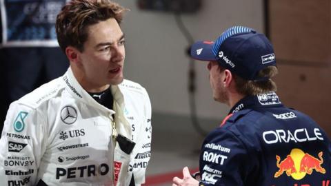 George Russell and Max Verstappen talk to each other in the pit lane