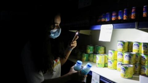 A women uses her phone light in a shop in Lebanon during a power cut