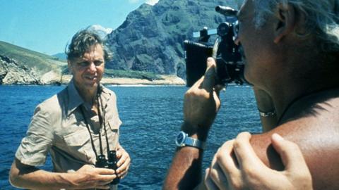 Sir David Attenborough being filmed in front of the sea and mountains for Life on Earth in 1979