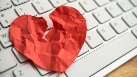 A paper heart which is torn and crumpled on top of a white computer keyboard.