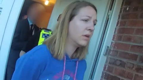 Screen grab taken from video footage shot by Cheshire Police after they had arrested Lucy Letby. Letby, with long blonde hair, is wearing a blue hoody as she is led from her house by officers.