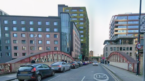 Google streetview of cars queuing on Irwell Street bridge with a six-storey hotel on the left and other high-rise buildings on the right