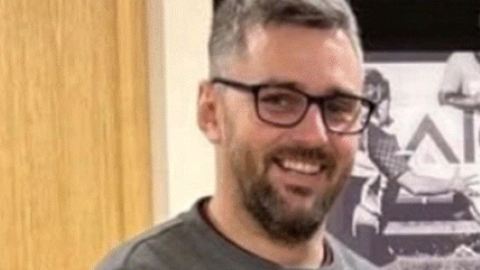 A blurry image of Craig Hurcombe who is smiling at the camera. He has a dark beard and glasses
