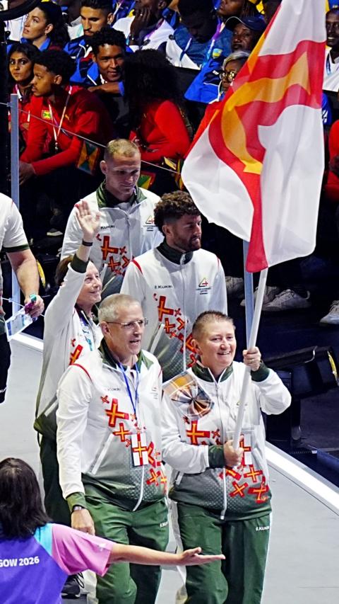 People dressed in white and green tracksuits and holding a Guernsey flag on a pole