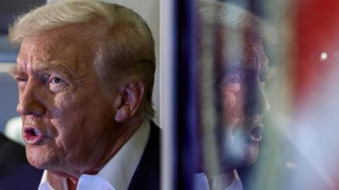 President Trump is seen speaking to reporters on board Air Force 1 with his image reflected in a monitor.
