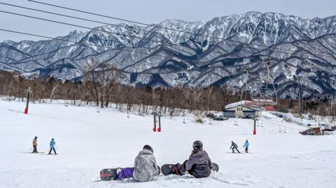  Snowboarders at the top of a ski slope with jagged mountain background 