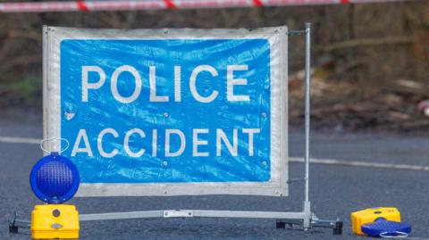 A close-up of a "Police accident" sign, with two blue lights on the ground next to it. One has fallen over.