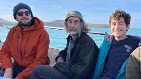 Three men on a boat with a turquoise sea in the background