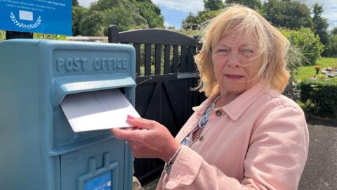 A woman posts a letter in a bright blue postbox 