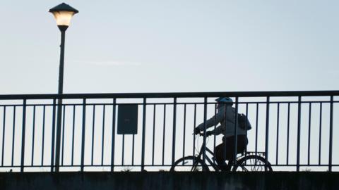 Cyclist on Donnington Bridge, seen from the Thames Path below. There is a lit lamp on the bridge.