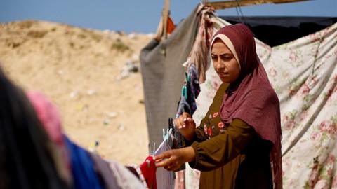 A displaced Palestinian woman stands with laundry at a tent camp in Rafah