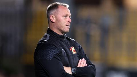 Michael Flynn with his arms folded on the touchline at a Swindon match