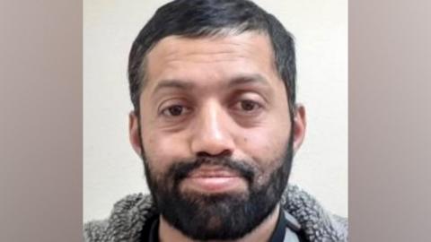 Malik Faisal Akram, with dark hair and a beard, wears a coat with a grey fur collar