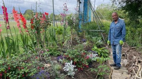 A man stood next to a planter containing plants and flowers inspired by Caribbean heritage.