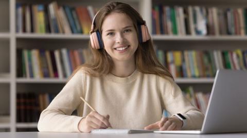 GCSE English Literature student wearing headphones in a library with laptop listening to Bitesize podcast