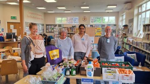 Four volunteers stood in front of desks of food