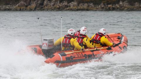 A lifeboat speeds across the water with four crew in bright yellow outfits on board