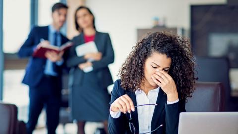 A woman in the workplace under pressure, as two colleagues talk behind her back