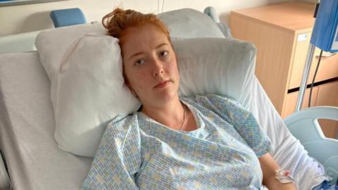 A woman with red hair in hospital clothing, lying in a hospital bed