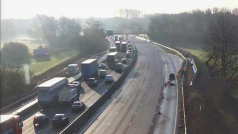 A traffic camera image of the M1 carriageway in Northamptonshire. One side of the carriageway is heavily congested with vehicles queuing while the other side is empty of vehicles. 