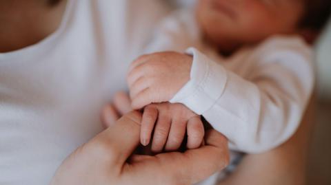 A close up of an adult holding a baby, both in white, while holding hands