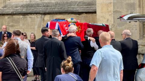 The coffin of Martin Chadburn draped with a military flag is carried into Hull Minster while mourners look on