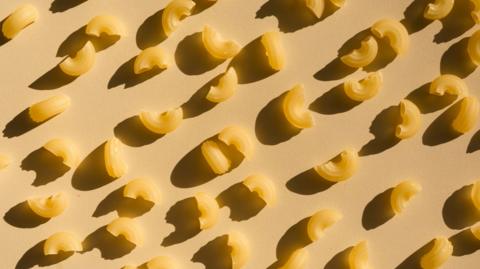 Pieces of dry pasta on a beige brackground with shadows