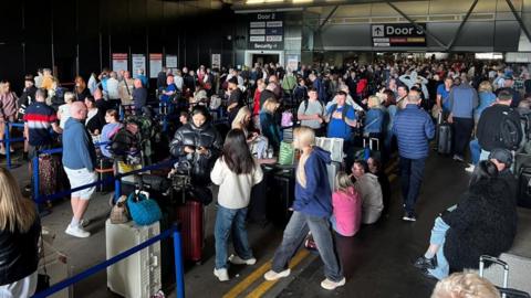 Passengers queue at the Manchester Airport after a power outage caused flights to be cancelled.