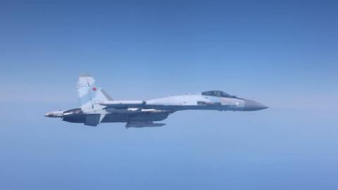 A grey Russian fighter jet is flying against a clear blue sky.