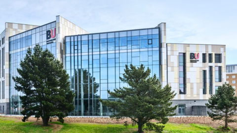 Bournemouth University glass building with two BU signs and three trees in front of the campus.