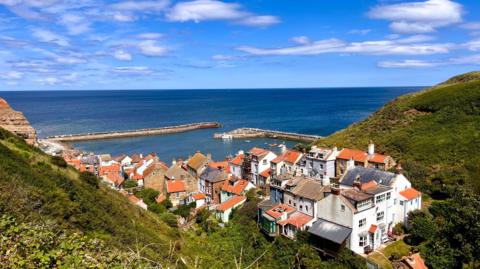 A view over a pretty coastal village looking out over a small harbour towards the sea, under a fairweather sky