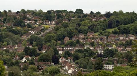 A picture of Wycombe, showing houses on the side of a hill and also a number of trees in a valley.