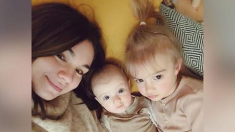 A mum smiles at the camera with her two young children