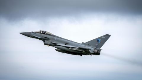 Grey jet aircraft with missiles under its wings pictured in an upward trajectory.