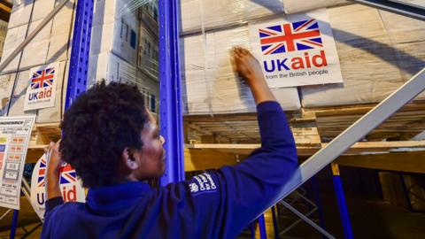 Logistics officer Beverley Sarpong places UK aid stickers onto cargo pallets containing British aid items destined for areas suffering humanitarian crisis at DFID &UK Disaster Response Operations Centre at Cotswold Airport, Kemble.
